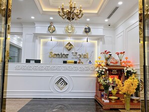 A hotel reception desk with a marble countertop, a chandelier, and a clock above it. - Senior Hotel (Can Tho)