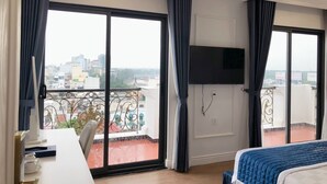 A hotel room with a balcony, a bed, a TV, and a desk with a chair. - Senior Hotel (Can Tho)