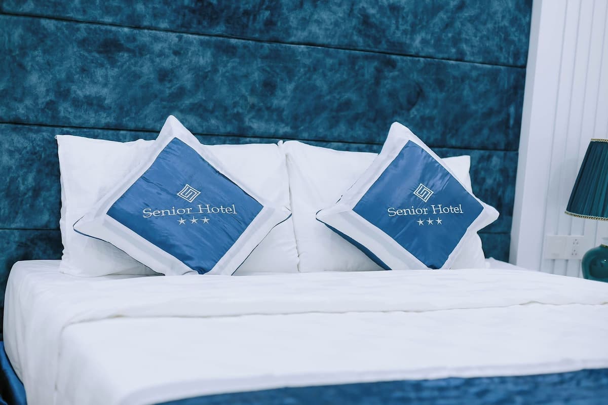 Una cama con ropa de cama blanca y dos almohadas con el logotipo 'Senior Hotel'.