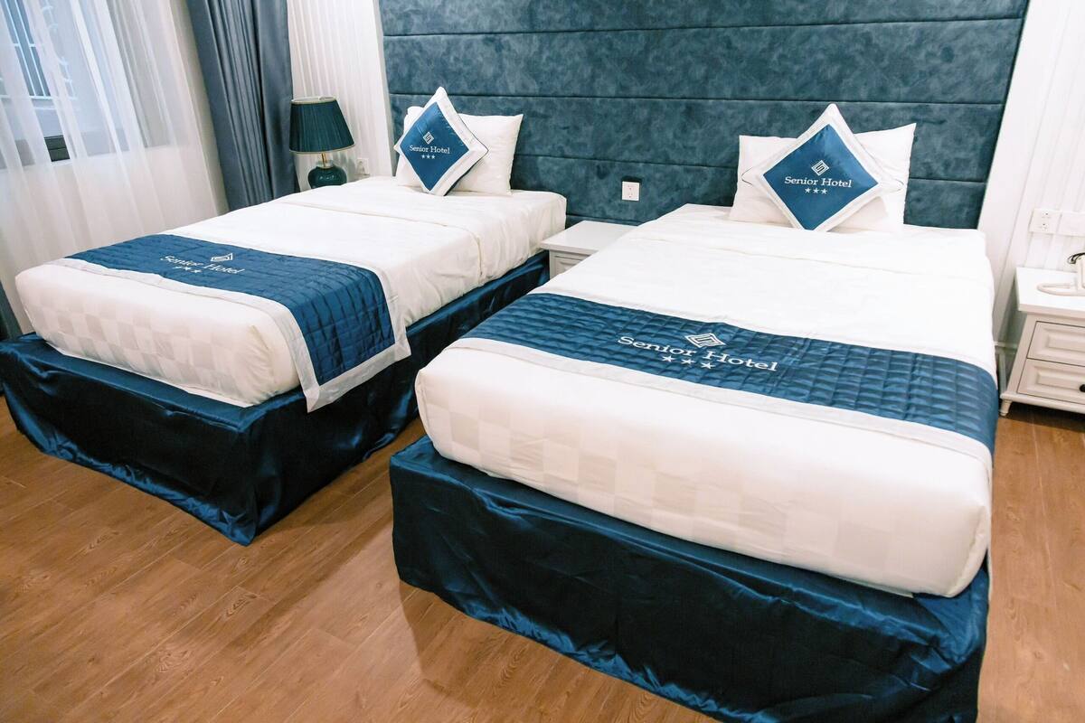 Habitación de hotel con dos camas, cada una con colcha y almohadas azules, y cabeceros azul oscuro.