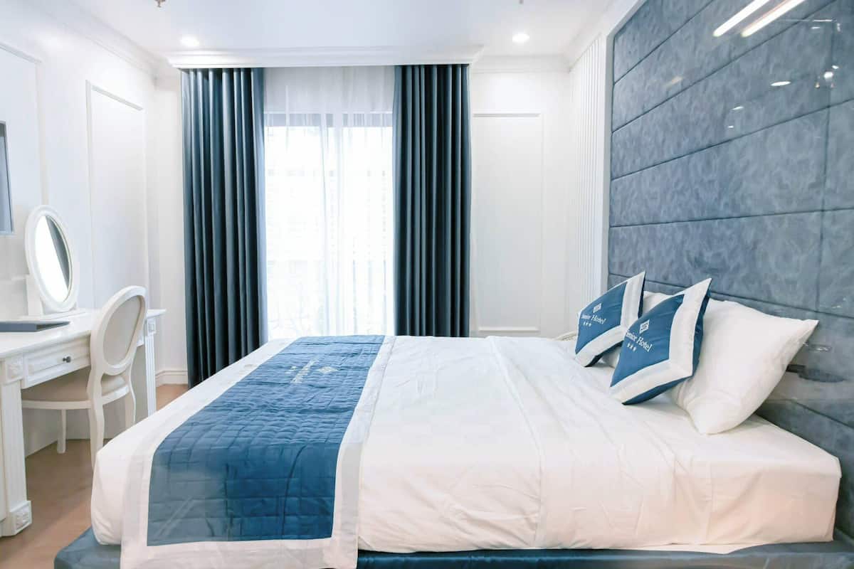 Habitación de hotel con cama, escritorio, silla, espejo y vistas al exterior.