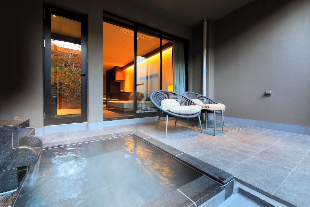 Una habitación de hotel moderna con un ventanal que da a un balcón, una bañera de hidromasaje y dos sillas de mimbre.
