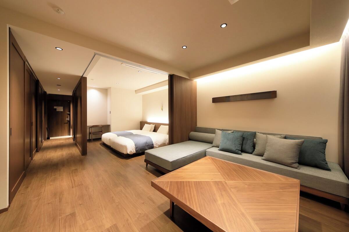 Una habitación de hotel moderna con suelo de madera, un sofá, una cama y una mesa de centro de madera.