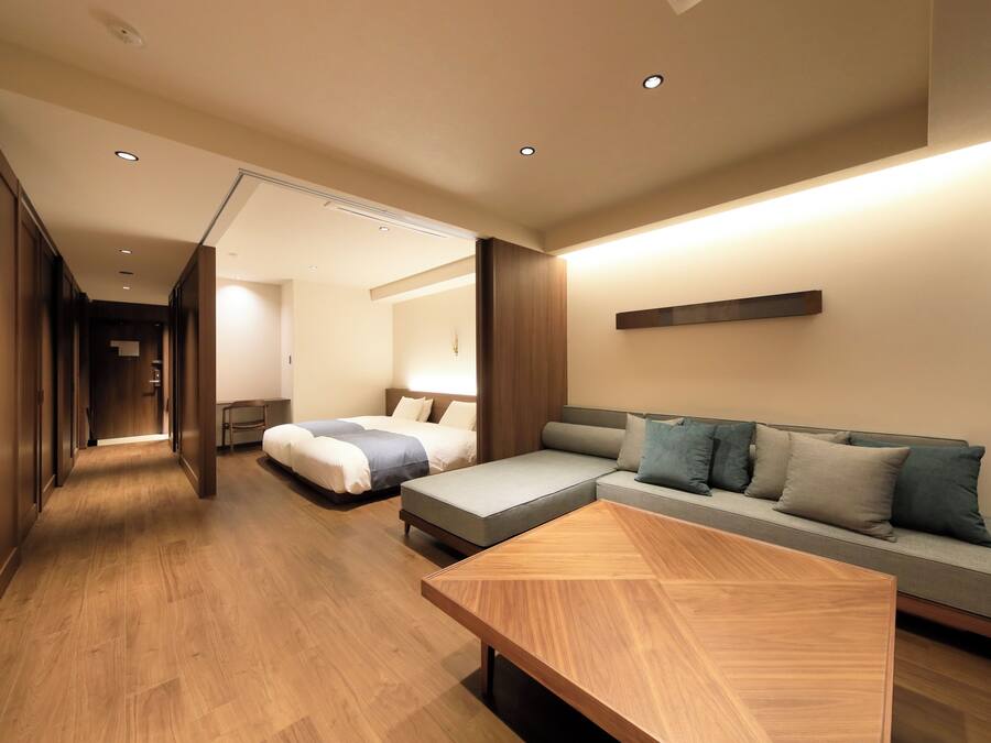 Quarto de hotel moderno com piso de madeira, um sofá, uma cama e uma mesa de centro de madeira.