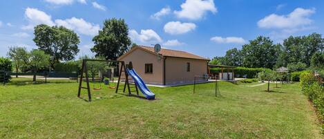 A house with a backyard containing a swing set and a slide.