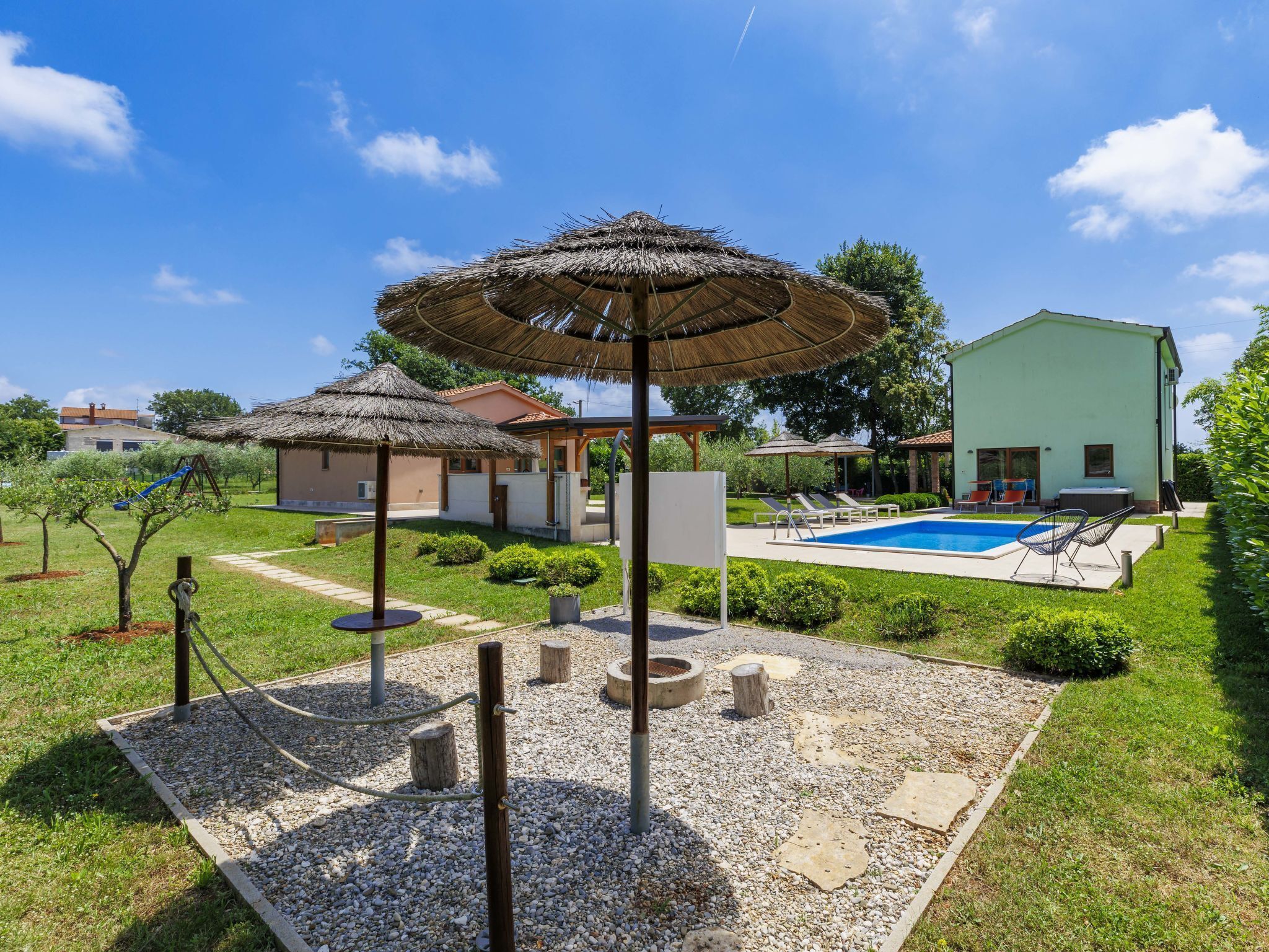 Un jardin avec une piscine, un espace salon couvert et une petite structure de jeux pour enfants.