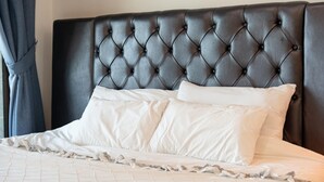 Ein Bett mit einer gepolsterten Kopfteil, weißer Bettwäsche und einem gerafften Bettvorhang.