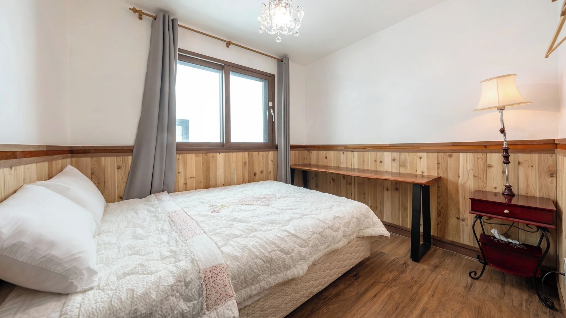 A bedroom with a bed, a nightstand, a lamp, and a window with curtains.