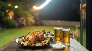 Pollo asado con verduras y dos jarras de cerveza sobre una mesa.