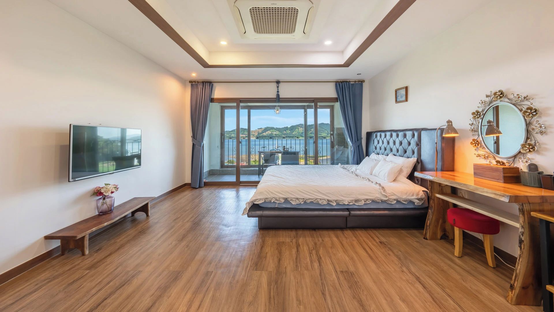 Un dormitorio con cama, escritorio, televisor y vistas al exterior.