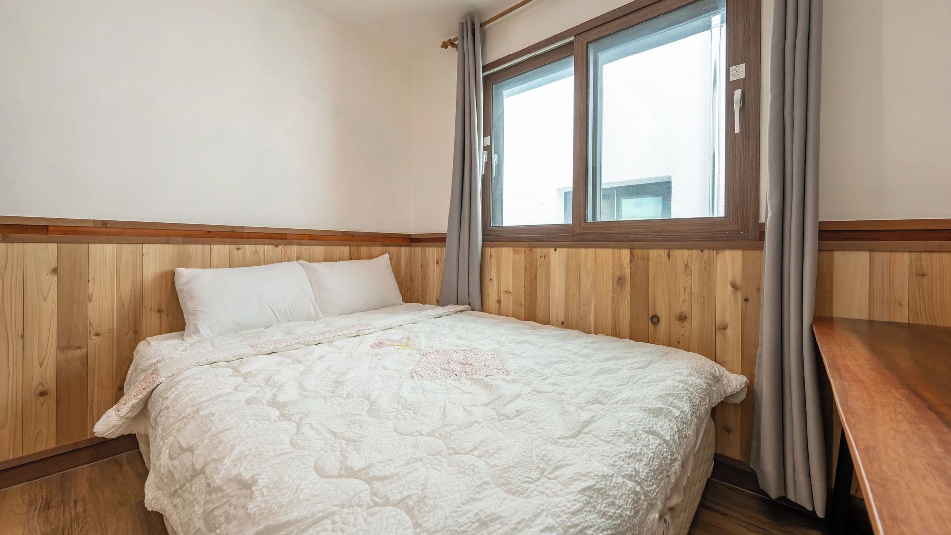 Ein Schlafzimmer mit einem Holzkopfteil, einem Bett mit einer Steppdecke, einem Fenster mit Vorhängen und einem Nachttisch aus Holz.