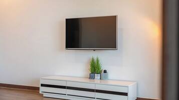 A modern living room with a flat-screen TV mounted on the wall, a white console table with drawers, and a small potted plant.
