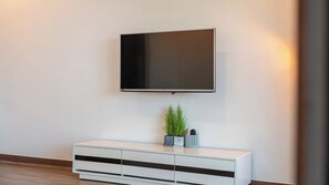 A modern living room with a flat-screen TV mounted on the wall, a white console table with drawers, and a small potted plant. - Namhae Ryu&lee Pet Pension (Namhae)