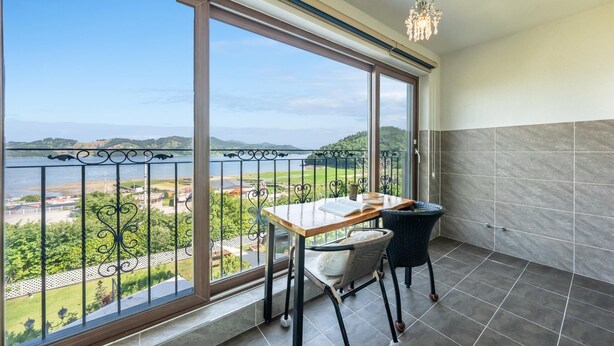 Ein Balkon mit Tisch und Stuhl, Blick auf ein Gewässer und Grünflächen, und ein Fliesenboden.