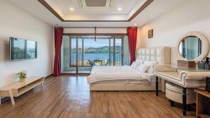 A bedroom with a large bed, a glass desk, a TV mounted on the wall, and a view of a body of water through the window. - Namhae Ryu&lee Pet Pension (Namhae)