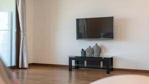 Una sala moderna con un televisor de pantalla plana montado en la pared, una consola de madera oscura con jarrones decorativos, y un ventanal con cortinas.