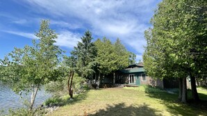 Una cabaña junto al lago con un patio cubierto de césped y árboles.