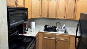 A kitchen with wooden cabinets, a microwave, a coffee maker, a digital clock, and a sink. - Cozy 1-bedroom apartment with WiFi, AC in wonderful Baton Rouge (Baton Rouge)