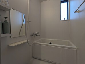 Een moderne badkamer met een witte badkuip, een handdouche en een raam dat voor natuurlijk licht zorgt.