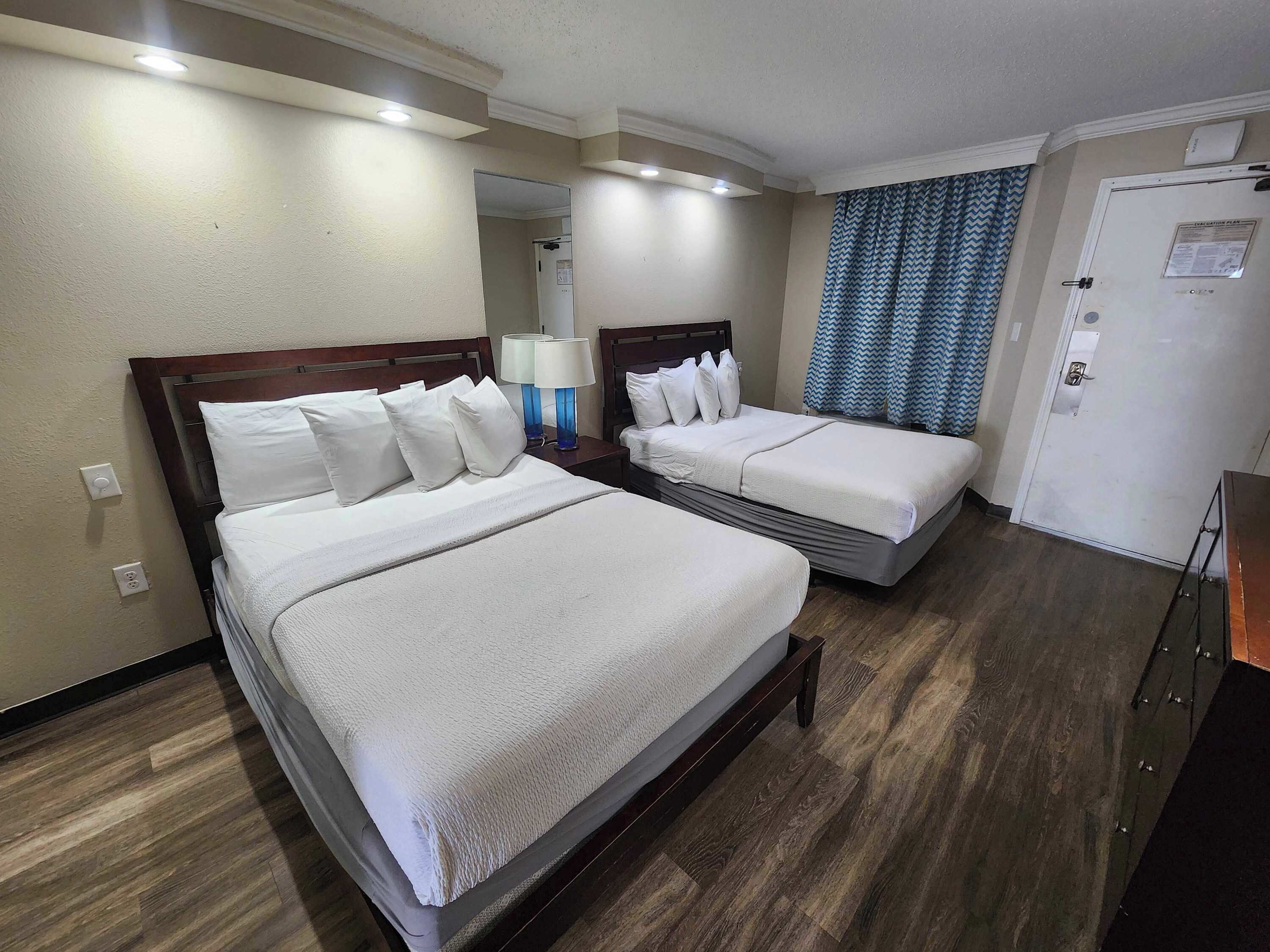A hotel room with two beds, a nightstand with lamps, a door with a notice, and a wooden floor.