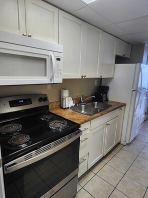 Una cocina con armarios blancos, una estufa negra, un microondas, un fregadero y un refrigerador.