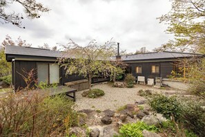 Ein modernes Haus mit Kiesweg, einer Holzterrasse und einem Garten mit Steinen und Pflanzen.