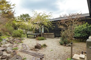 Ein Garten mit einer hölzernen Bank, einem Picknicktisch und einem gepflasterten Weg, der zu einem Gebäude mit dunkler Fassade führt.