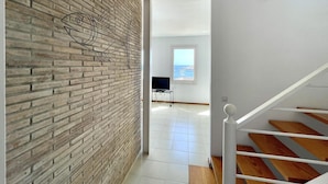 A modern interior with a brick wall, a staircase, and a view of the sea through a window. - Sa Tuna - House with Views and 30m from the Sea (Begur)