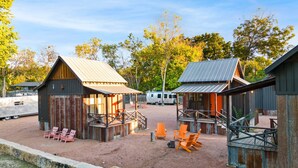 Um camping com cabanas de madeira rústica, área de estar externa e chão de terra.