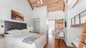 Quarto de hotel com uma cama grande, teto de madeira, televisão e um pequeno espaço para sentar.
