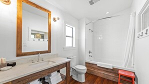Een badkamer met een houten wastafelmeubel, een wit toilet, een douche met glazen deur en een rode kruk.