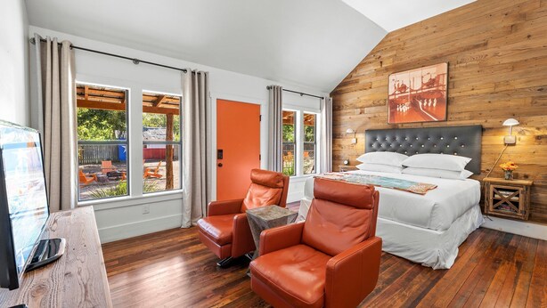 Een slaapkamer met een bed, twee leren fauteuils, een houten vloer, een raam met gordijnen en een houten wand.