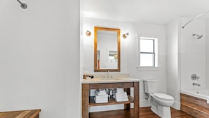 Een badkamer met een houten wastafelmeubel, een wit toilet en een douche.