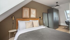 A bedroom with a sloped ceiling, a bed with white bedding, two framed artworks, a wardrobe, a desk with a chair, and a window. - Delightful Josefstadt 3BR, Furnished + Open Design, by Blueground (Vienna)