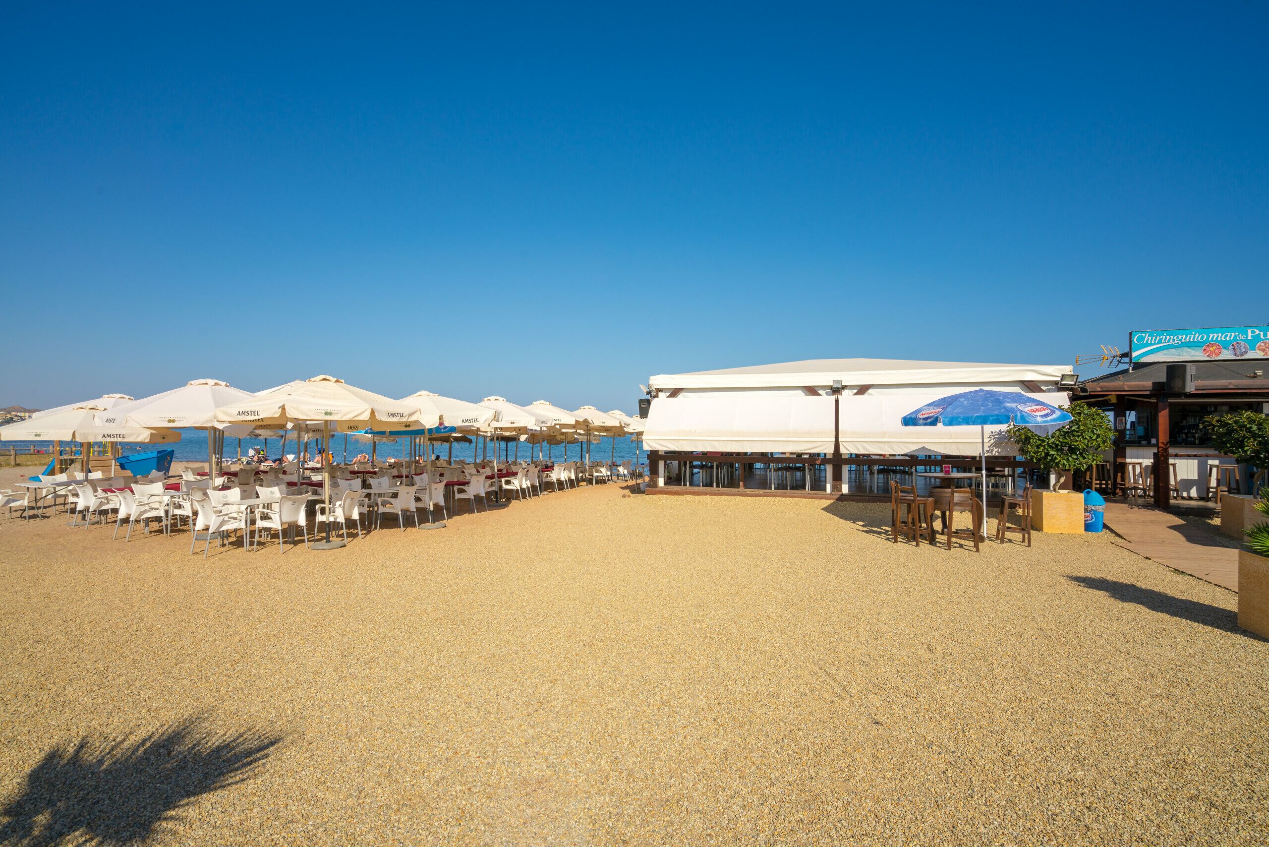 Un restaurante junto a la playa con terraza, sombrillas y vistas al mar.