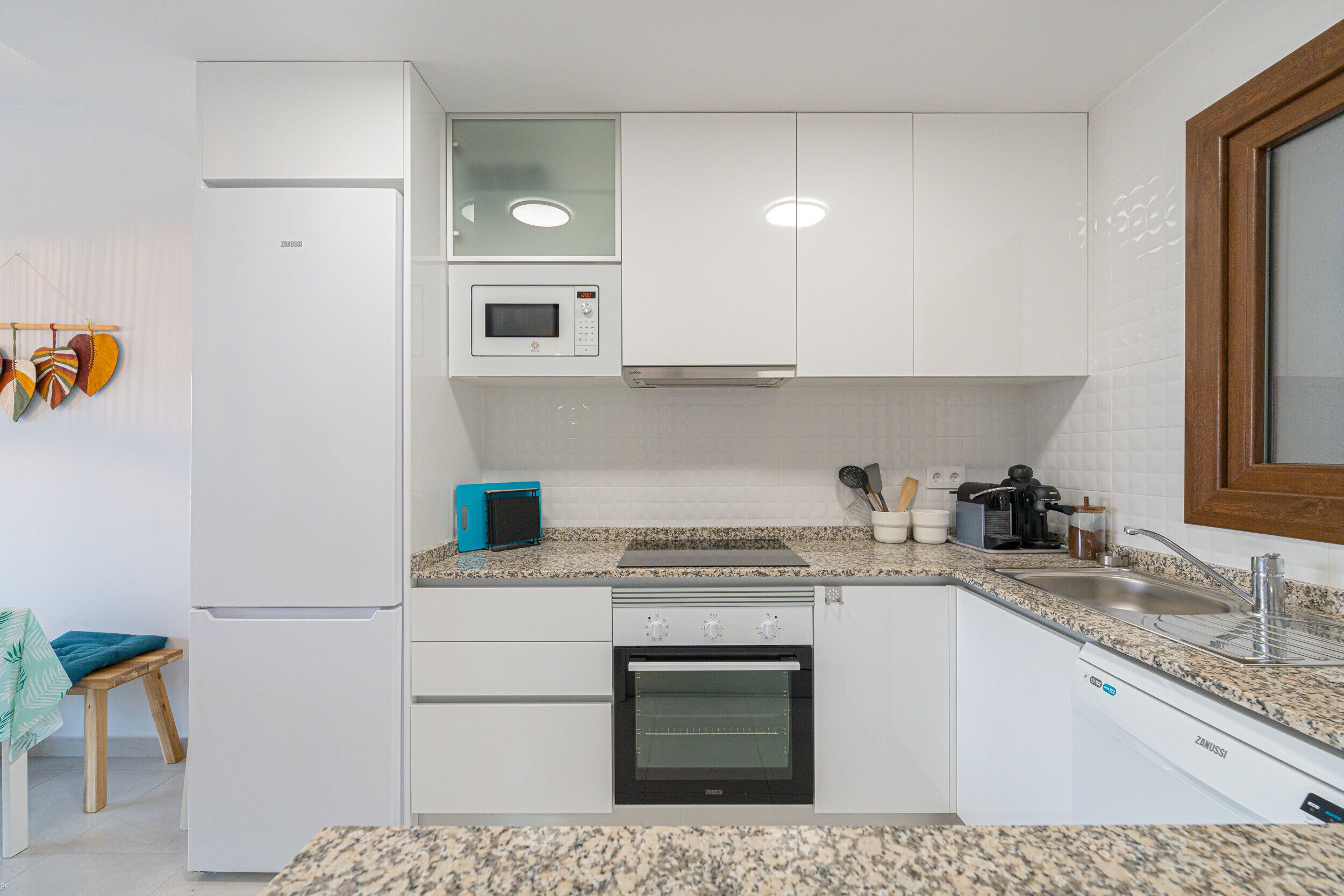 A kitchen with white cabinets, a microwave, a toaster, a sink, and a dishwasher.