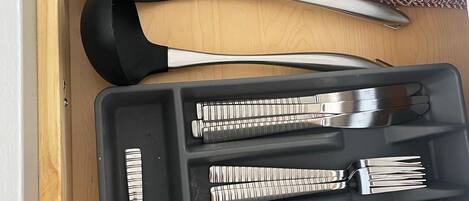 A drawer containing a knife, spatula, tongs, and a set of silverware including forks, spoons, and a knife.
