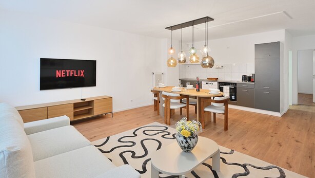 A modern living room with a flat-screen TV, a dining area with a wooden table and chairs, and a kitchen in the background. - Chic and Spacious 2Room Apartment in Wuppertal Center with Free WiFi and Kitchen (Wuppertal)