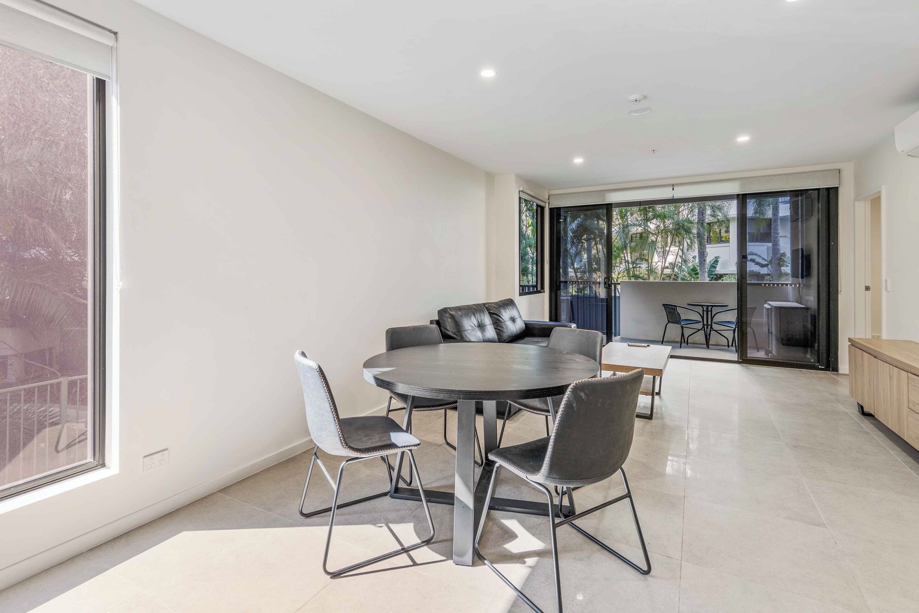 A modern dining area with a round table and chairs, large windows, and a view of the outdoors.