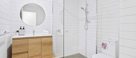 Een moderne badkamer met een douchecabine van glas, een houten wastafelmeubel en een toilet met een bloemendecoratie.