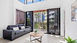 A modern living room with a sofa, a round coffee table, and a balcony with a view of tall buildings and palm trees. - The Aubrey Boutique Apartments (Surfers Paradise)