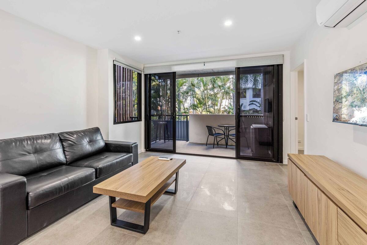 A modern living room with a black leather sofa, a wooden coffee table, and a wooden cabinet.