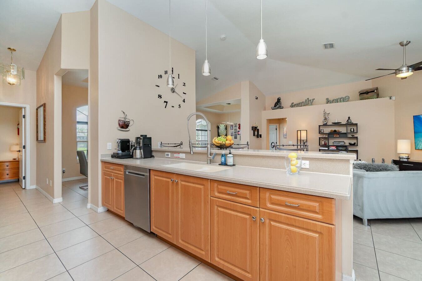 A modern kitchen with wooden cabinets, a dishwasher, and a large island with a sink. There is a fruit bowl on the island and a coffee maker on the counter.