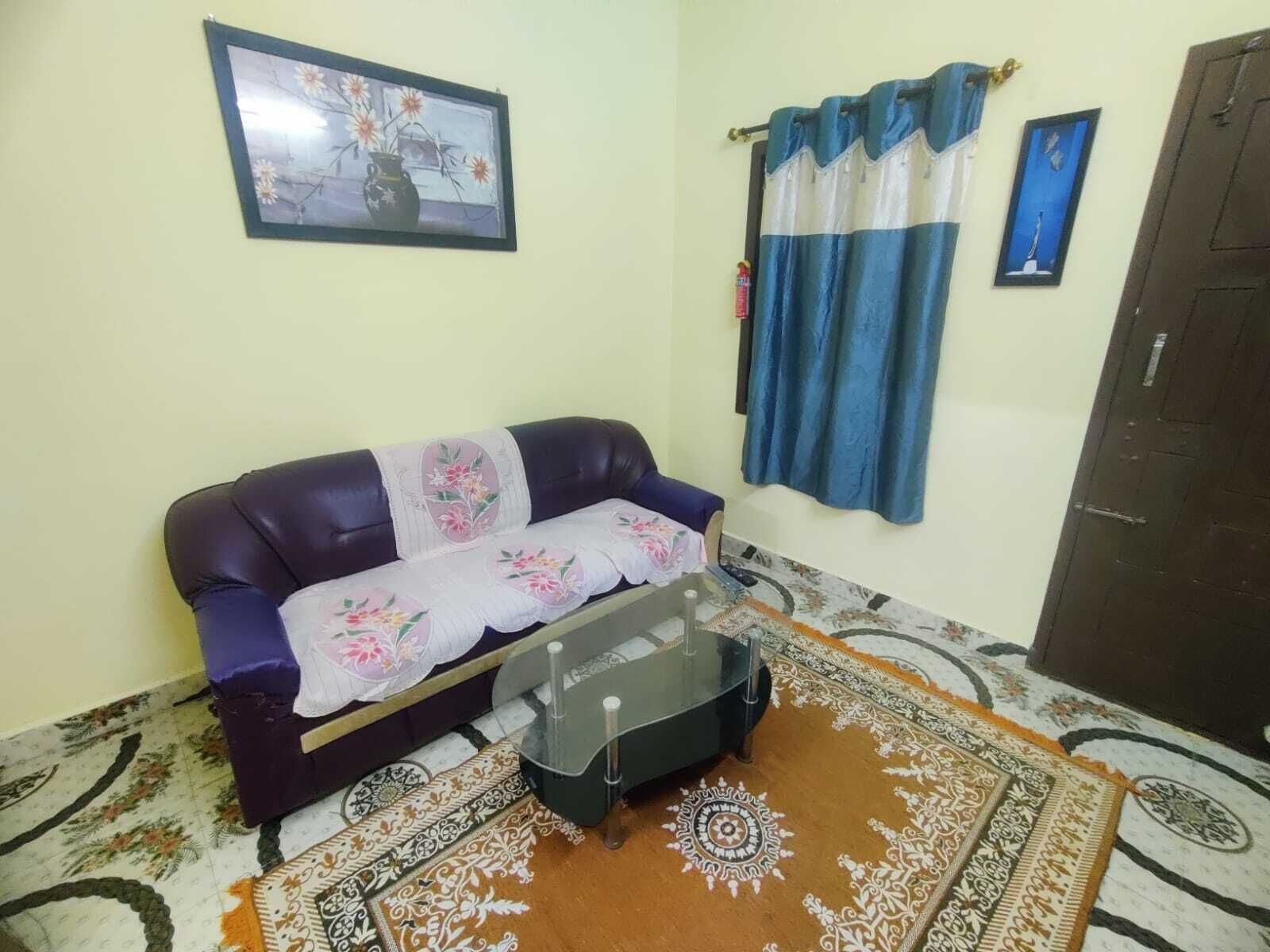 A living room with a sofa, a glass coffee table, patterned rugs, and curtains.