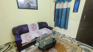A living room with a sofa, a glass coffee table, patterned rugs, and curtains.