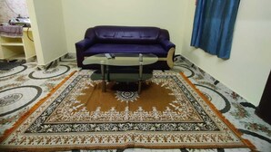 A living room with a purple sofa, a glass coffee table, and a patterned rug. - Feel at Home: Exceptional Comfort and Convenience! (Chennai)