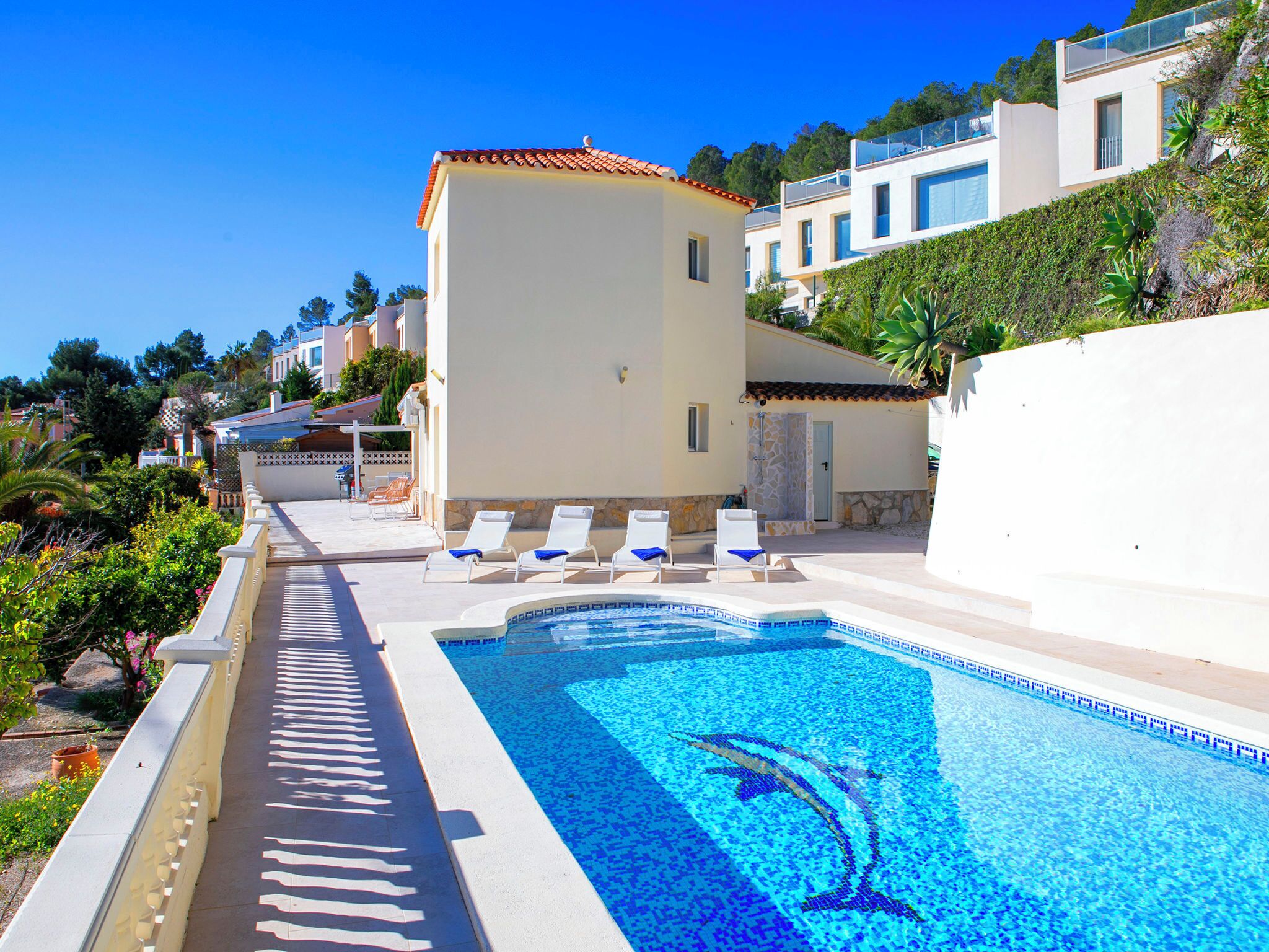 A pool with a dolphin design, white lounge chairs, and a clear blue sky.