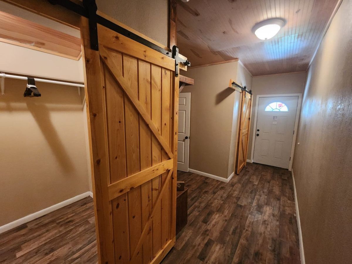 A narrow hallway with wooden flooring, a wooden door, and a small window with a stained glass design.