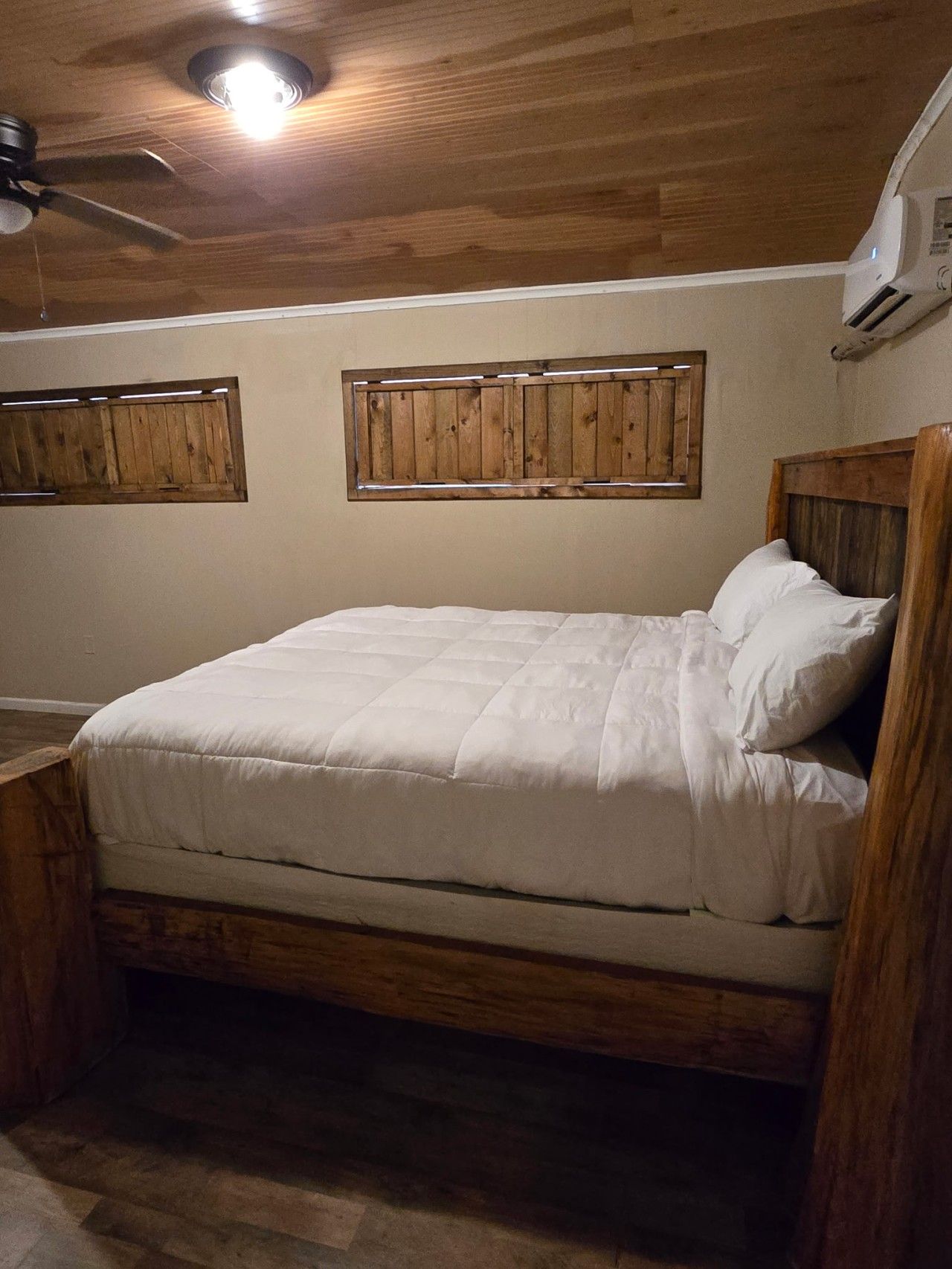Un lit simple avec une tête de lit et un pied de lit en bois, un ventilateur de plafond et un climatiseur fixé au mur.
