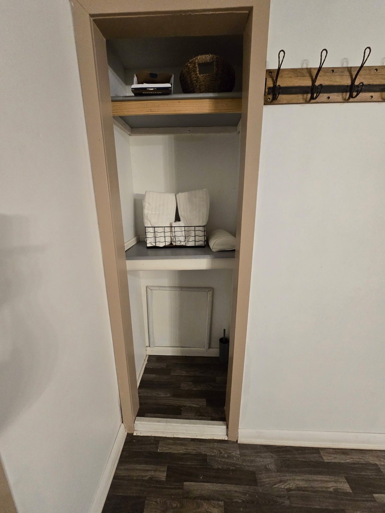 A narrow hallway leading to a closet with shelves, a basket, and a coat rack.